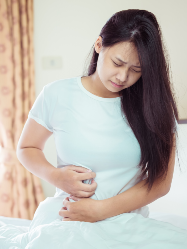 Donna con dolore allo stomaco seduta sul letto